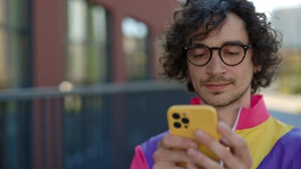 Мужчина хипстер в разноцветной куртке с помощью смартфона на открытом воздухе — стоковое видео