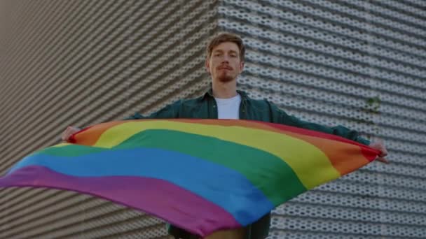 Portret van een blanke man met kleurrijke lgbt-vlag in handen terwijl hij op straat naar de camera keek. Beweging tegen discriminatie van homoseksuelen. Begrip solidariteit. — Stockvideo