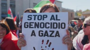 Rome, Italy, 5.10.2025: A protester holds a sign reading Stop al genocidio a Gaza during a demonstration supporting Palestine. People gather under bright sunlight in the city center.