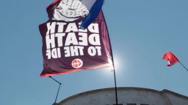 Rome, Italy, 5.10.2025: A black flag with the phrase Death to the IDF waves alongside others during a pro-Palestine protest under clear skies, expressing anger and political opposition.