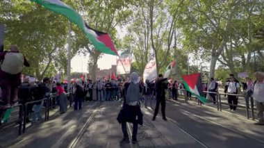 Rome, Italy, 5.10.2025: Protesters with Palestinian flags and banners march on the street during a large demonstration surrounded by trees and afternoon sunlight.