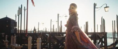 Venedik, İtalya - 05 Mart 2025: günbatımında iskelede altın maskeli kadın portresi. Klasik elbiseli zarif bayan şehrin seddi üzerinde pelerini sallıyor Anamorfik lens