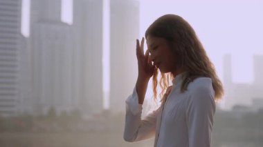 Beyaz elbiseli, gururlu Asyalı bir kadının portresi, şehrin rıhtımındaki kılları düzeltiyor. Romantik Taylandlı lezbiyen kameraya bakıyor ve setin kenarındaki gökdelenlerin önünde dikiliyor.