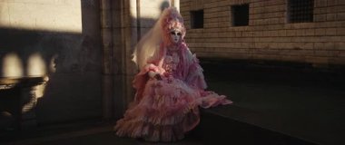 VENICE, ITALY - MARCH 05 2025: Portrait of woman in pink carnival costume decorated with lace and veil at St Mark Square. Cryptic lady in festive dress with mask in town at twilight anamorphic lens