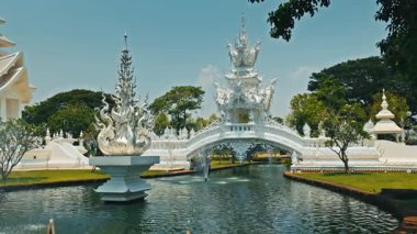 CHIANG RAI, THAILAND - Eylül 04 2025: temiz nehir Beyaz Tapınak 'ta zarif bir köprü altında süzülüyor. Çeşmeler suyu havaya püskürterek tropik güneşin altında parlayan bir sis oluşturur.