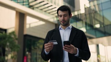 Genç İspanyol iş adamının portresi, iş merkezinin yakınındaki akıllı telefondan banka uygulaması ile ödeme yapıyor. Latin bir adam, şehir merkezinde online para transferi için kredi kartı kullanıyor. E finans