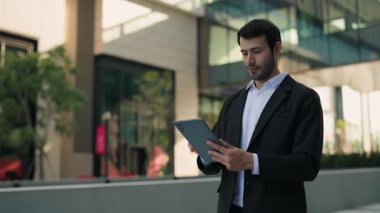 İspanyol erkek yöneticinin portresi ofis merkezinin yakınındaki dijital tablete internet yüklüyor. Latin girişimci, finans bölgesinde piyasa eğilimlerini mobil cihazla İnternet üzerinden kontrol ediyor