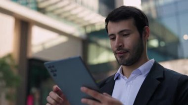 İspanyol tüccarın portresi ofis merkezinin dışındaki dijital tablette internette sörf yapıyor. Genç Latin işadamı, mali bölgede dururken cep telefonundan e-postaları okuyor