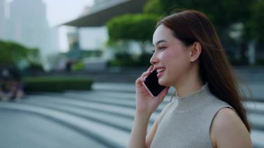 Mutlu Asyalı kadın portresi akıllı telefondan şehir meydanında ağır çekimde yürürken konuşuyor. Genç esmer Koreli kadın Megapolis bölgesinde cep telefonuyla kız arkadaş arıyor.