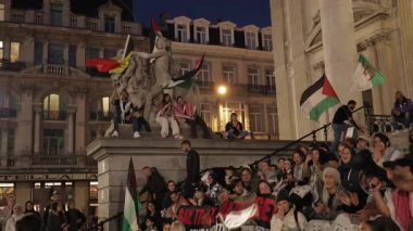 BRÜKSEL, BELGIUM - 27 Eylül 2025: Gürültücü protestocular Bourse de Bruxelles yakınlarındaki basamaklarda akşam ağır çekimde ulusal Filistin bayraklarını sallıyorlar. Kalabalık AB 'de Filistin' e destek gösteriyor