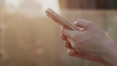 Günbatımı caddesinde genç kadın ellerinin ekili görüntüsü modern akıllı telefonu tutuyor. Dışarıdaki cep telefonuyla dokunmatik ekranı dinleyerek arkadaşa kadın mesajları. Dijital iletişim teknolojisi