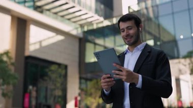 Mutlu İspanyol girişimcinin portresi dijital tablet aracılığıyla iş arkadaşlarıyla görüntülü konuşma yapıyor. Latin yönetici açık havada görüntülü sohbet ortaklarıyla yenilikleri tartışıyor