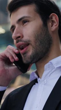 Mutlu İspanyol adam portresi şirket çalışanı cep telefonuyla dikey çekim yapıyor. Genç Latin iş uzmanları, modern şehrin telefon görüşmesinde müşterilerine danışıyor.