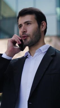 Neşeli İspanyol menajerin portresi şirket binasının yakınlarında cep telefonuyla dikey çekim yapıyor. Genç sakallı Latin işadamı modern şehirde telefonla konuşuyor.