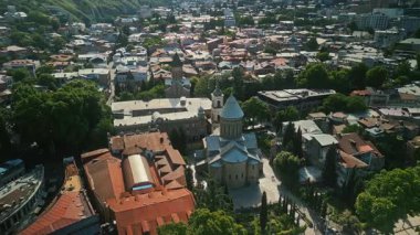 Gürcistan 'ın başkenti Tiflis' te mimari güzellik ve kentsel yaşamı gözler önüne seren yemyeşil ağaçlar ve renkli çatılarla çevrili tarihi bir kilisenin hava manzarası.