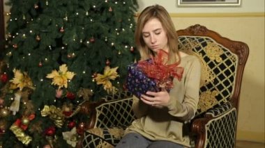 Güzel kız Noel hediyesine bakarak kasa ve kameraya doğru görünüyor