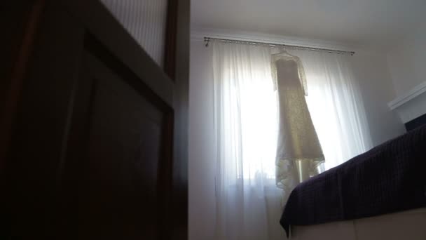 Beautiful wedding dress hanging in a window. young bride approaches the window — Stock Video