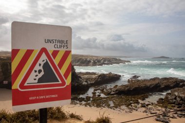 Coastline with warning cliff sign, Porto Covo, Sines, Portugal. clipart