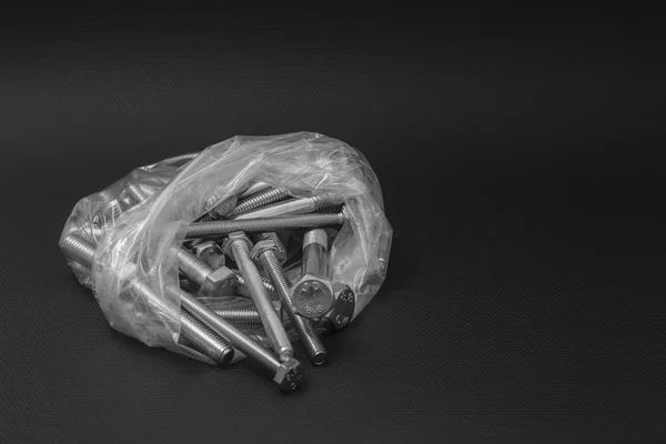 Boulons dans un sac en plastique transparent sur fond noir — Photo