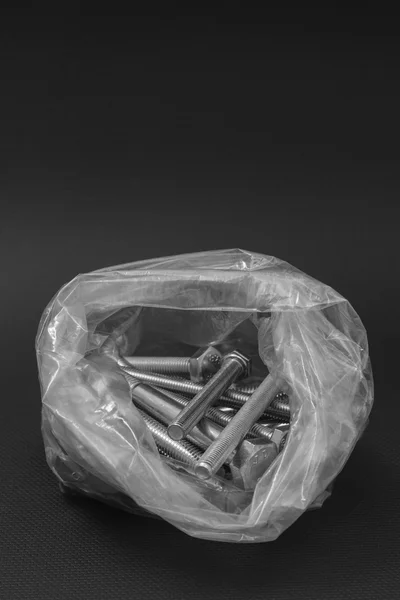 Boulons dans un sac en plastique transparent sur fond noir — Photo