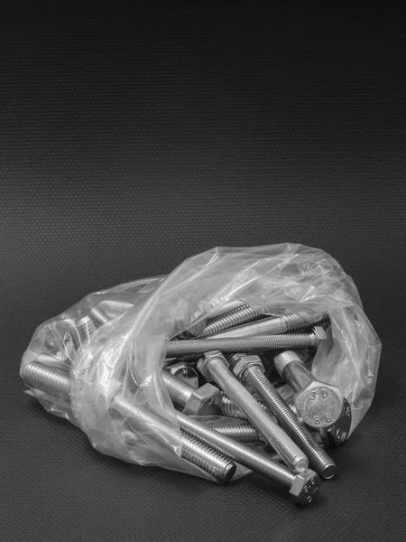 Parafusos em um saco de plástico transparente em um fundo preto — Fotografia de Stock