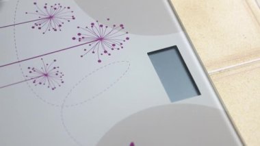 Kadın kendini elektronik ölçekte tartıyor.