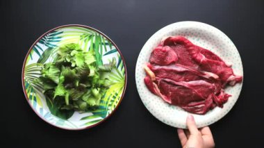 Siyah arka planda bir tabak et salatasını tercih eden bir el.