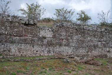 Paestum arkeolojik alanının antik taş duvarları dramatik gökyüzü altında.