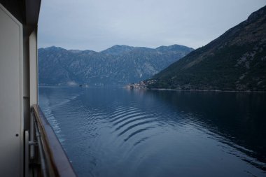 Kotor Körfezi 'nden geçen bir yolcu gemisi dağları ve uzak kıyı kasabasını görüyor.