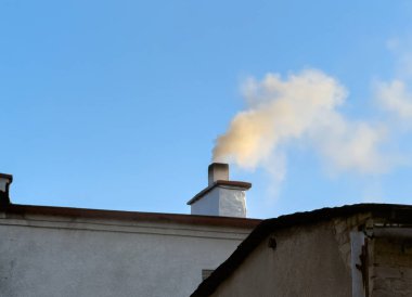 Banliyö ortamında ev ısıtma, hava kirliliği ve kış enerjisi kullanımını gösteren, çalışan bir ocak veya fırından yoğun ve ağır dumanlar çıkaran bir ev bacası..