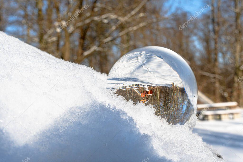 Glass ball or lens ball in the snow. The background with trees and other objects is reflected in the glass ball