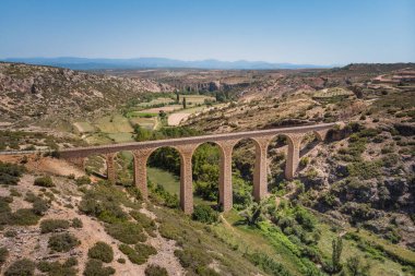 Hava görüntüsü, taştan köprü, güneş ışığında yeşil bir vadi boyunca uzanıyor. Yeşil yol, Teruel, İspanya.