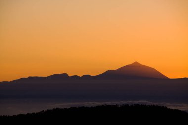 Güneş batarken Teide volkanının silueti Gran Kanarya 'dan sıcak turuncu tonlarda görüldü.