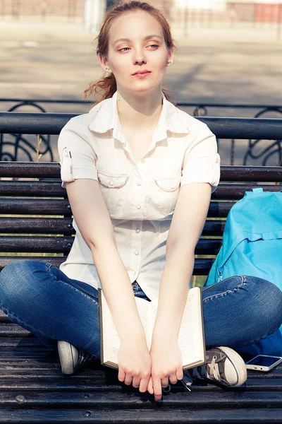 Chica joven con un libro sentado en un banco —  Fotos de Stock