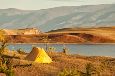 Resimli bir dağ gölünün kıyılarında sarı üçgen çadır, turizm ve kamp..