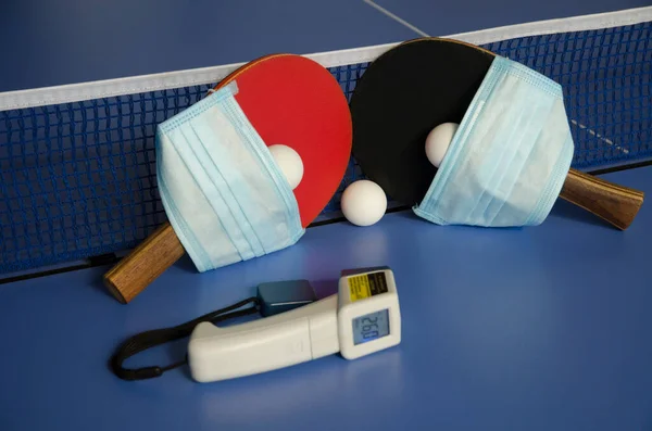 Table Tennis Paddles and ball on the blue table tennis table with medical mask and non-contact thermometer. Fitness and coronavirus