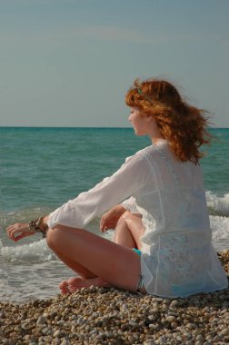 Genç güzel kızıl saçlı kız meditasyon yapıyor, denizin enginliğine bakıyor. 