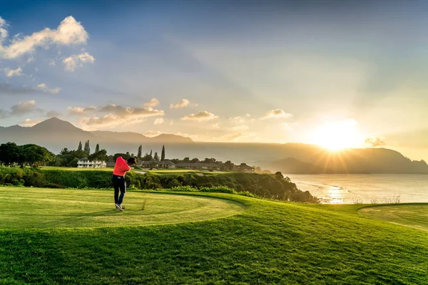 Tek moda golfçü Hawaii tropiklerinde okyanus kenarında gün batımına doğru golf oynuyor. Okyanusa yansıyan altın güneş ışınlarıyla çekilen çimento hareketi