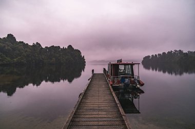 Sisli bir sabahta kasvetli bir rıhtım ve yalnız bir tekne.