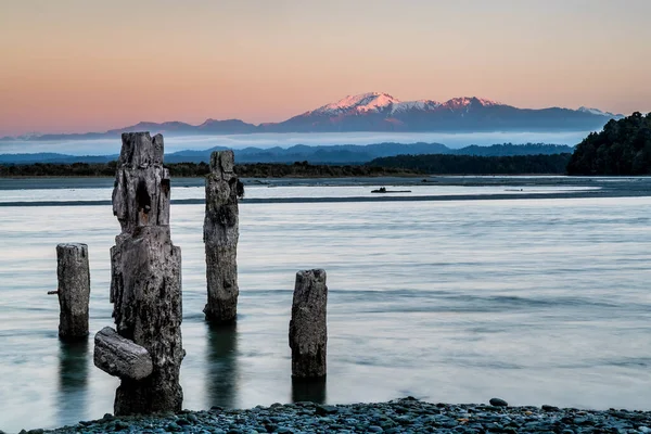 Uzun pozlama gündoğumu dağ arkaplanı ve ön planda harap olmuş eski rıhtım hepsi bir su turkuaz gölüne kurulmuş.