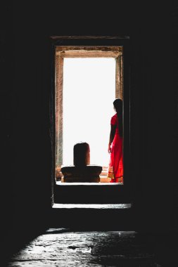 Parlak güneşli, kırmızı elbiseli bir Hindu kadın antik taş kalıntılarının içinden beyaz uçuruma bakıyor.