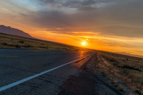 Gün batımında karanlık bir çöl otoyolu boyunca batan güneşin sanatsal açıdan çekilmiş bir fotoğrafı.