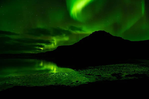 Raudasandur Dağı gecesi, yukarıdaki kuzey ışıklarını vurdu ve aşağıdaki suya yansıdı.