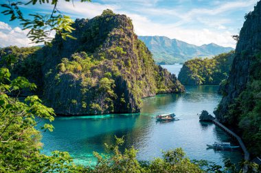 Güneşli bir günde Tropikal Filipinler Gölü manzarası. Bir tekne turistlere inanılmaz kaya oluşumlarını, tropikal ormanları ve kristal berrak turkuaz suları göstermek için aylak aylak dolaşıyor.