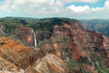 A small waterfall is almost eclipsed by the dramatic red rock of the Hawaiian Waimea Canyon. Called the Grand Canyon of the Hawaiian Islands, it is one of the most visited national parks and recreational areas in Kawaii, rivaling it's hollywood compe clipart