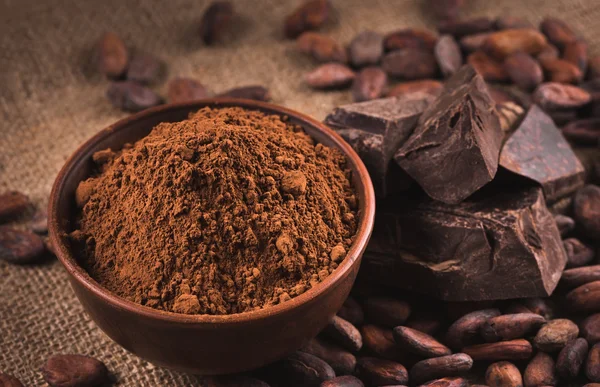 Granos de cacao crudos, tazón de barro con cacao en polvo, chocolate en saco —  Fotos de Stock