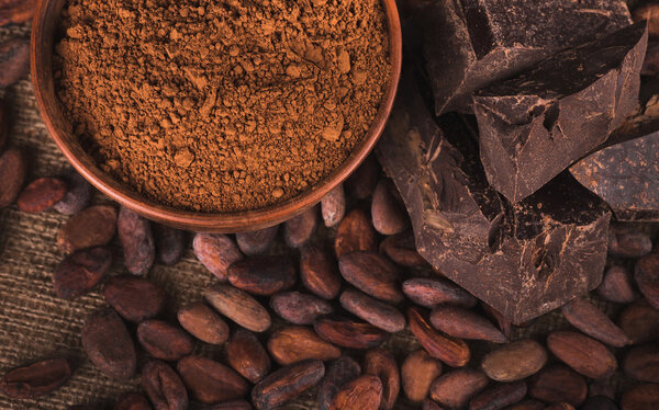 Raw cocoa beans, clay bowl  with cocoa powder, chocolate on sack