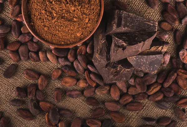Granos de cacao crudos, tazón de barro con cacao en polvo, chocolate en saco —  Fotos de Stock