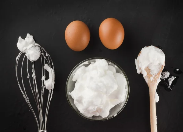 Whipped egg whites for cream in a glass bowl, whisk and wooden s