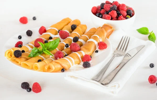 Sweet crepes rolled in a tubes decorated cream and ripe berries — Stock Photo, Image